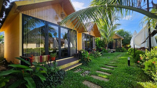 Un resort tropical con arquitectura moderna, amplios ventanales y un exuberante jardín con palmeras y un sendero.