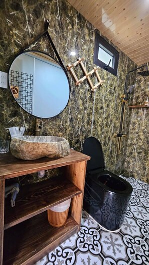 A bathroom with a wooden vanity, a round mirror, a black toilet, and a patterned floor. - Family Bungalow 2 Side by Side (Hoi An)