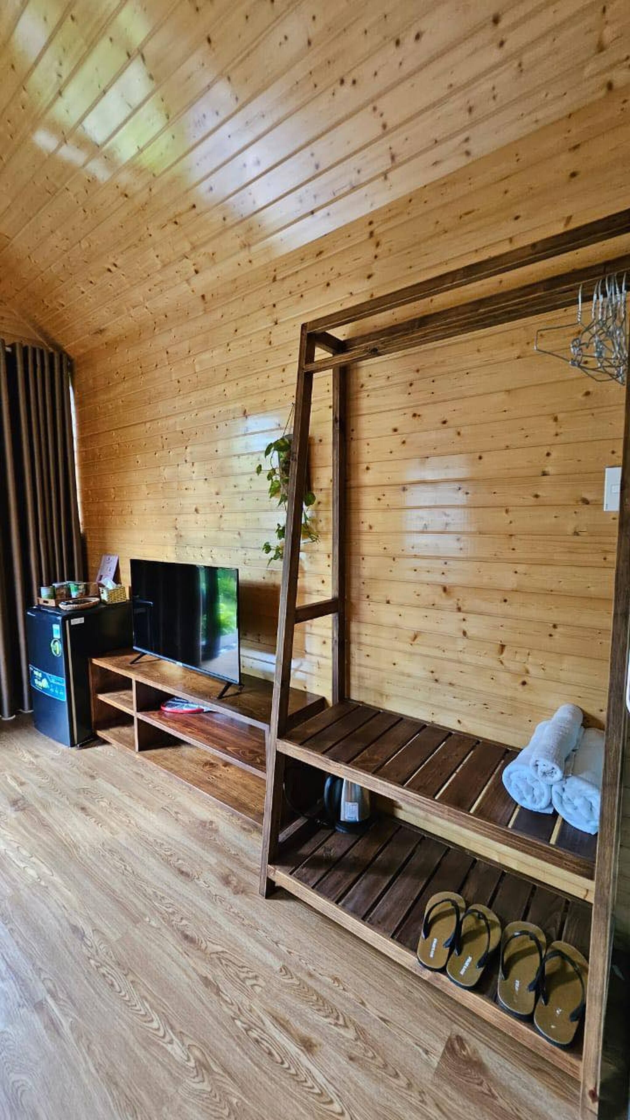 A wooden cabin room with a bunk bed, a TV, a small desk, and a shelf with slippers.