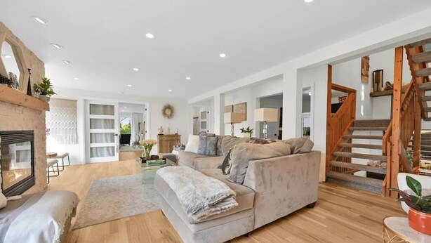 A spacious living room with a large sofa, a fireplace, wooden flooring, and a staircase leading to an upper level. - Riverfront Estate in Paris, 5 luxury Suites indoor pool hot tub self serve spa (Brant)