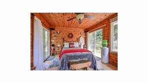 A wooden cabin bedroom with a bed, a ceiling fan, a window with a view, and a water dispenser. - Riverfront Estate in Paris, 5 luxury Suites indoor pool hot tub self serve spa (Brant)