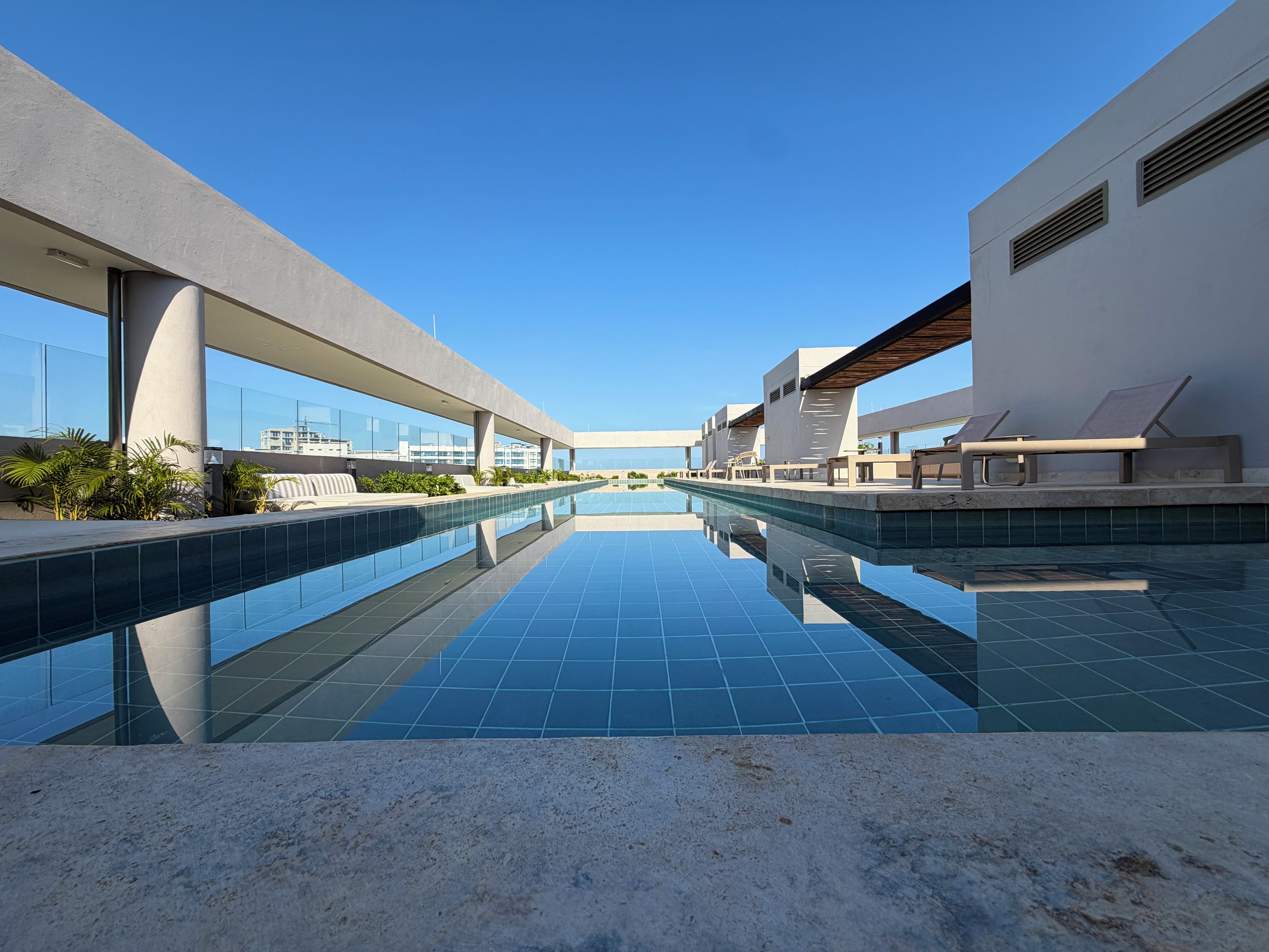 A modern pool area with clear blue water, lounge chairs, and a view of the city skyline.