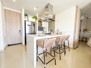 A modern kitchen with a central island, bar stools, a stainless steel refrigerator, and a microwave. - New Eco-Luxury Apt, Resort & Beach steps from the beach (Gaira)