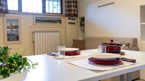 A dining table set with plates, glasses, and cutlery, a red pot on a coaster, and a plant on the table. - Modern & Practical Studio in Sauze d'Oulx (Sauze d'Oulx)