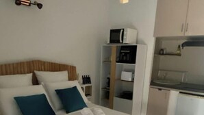 Hotellihuone, jossa on sänky, pieni keittonurkkaus ja valkoinen vaatekaappi.
