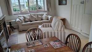 Ein Essbereich mit einem Holztisch, der mit Zeitschriften, einer Couch und einem gestreiften Stuhl im Hintergrund dekoriert ist.
