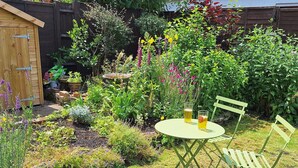 Ein Garten mit Tisch und Stühlen, umgeben von verschiedenen Pflanzen und Blumen.