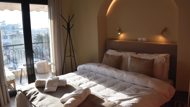 Ein Hotelzimmer mit einem großen Bett, Blick auf die Stadt durch das Fenster und einem Balkon mit Stuhl und Tisch.