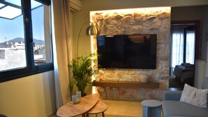 Ein modernes Wohnzimmer mit Kamin aus Stein, einem Flachbildfernseher, einem runden Holztisch und einer gemütlichen Couch.