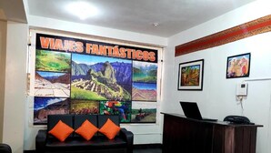 Een receptiegedeelte met een zwarte bank, oranje kussens, een houten bureau en een muur versierd met reisposters.