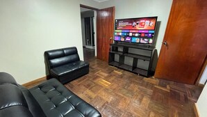 Een woonkamer met een zwarte leren bank, een houten visgraatvloer, een televisie op een houten dressoir en een houten deur.