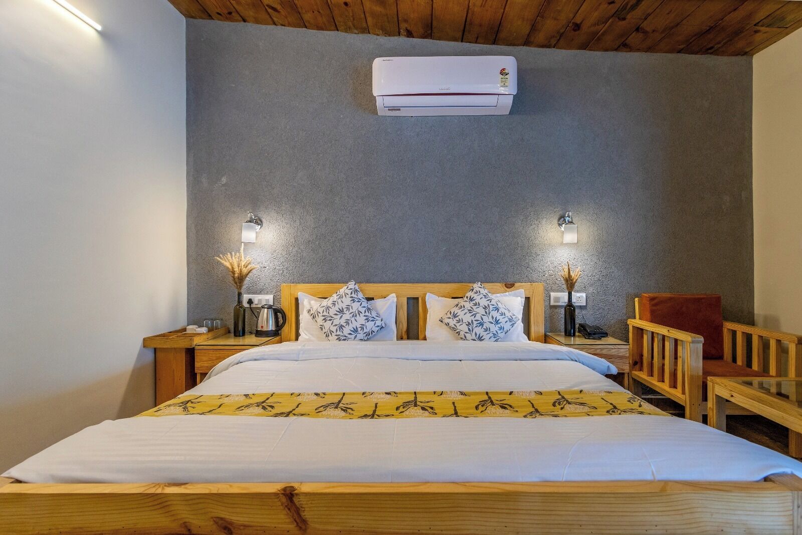 Ett hotellrum med en säng i trä, två sängbord med lampor, en röd stol och en luftkonditioneringsanläggning på väggen.