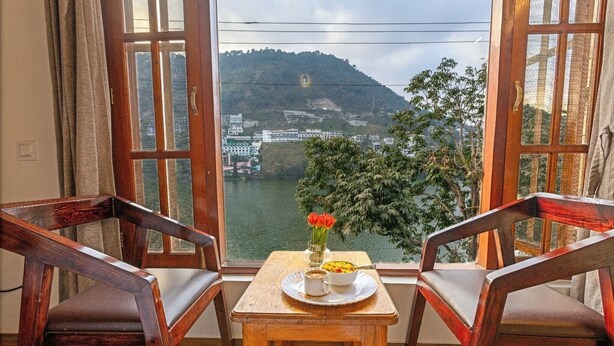 A room with two wooden chairs facing a window overlooking a river and a hill. - Dimmys By the Lake Bhimtal (Bhimtal)
