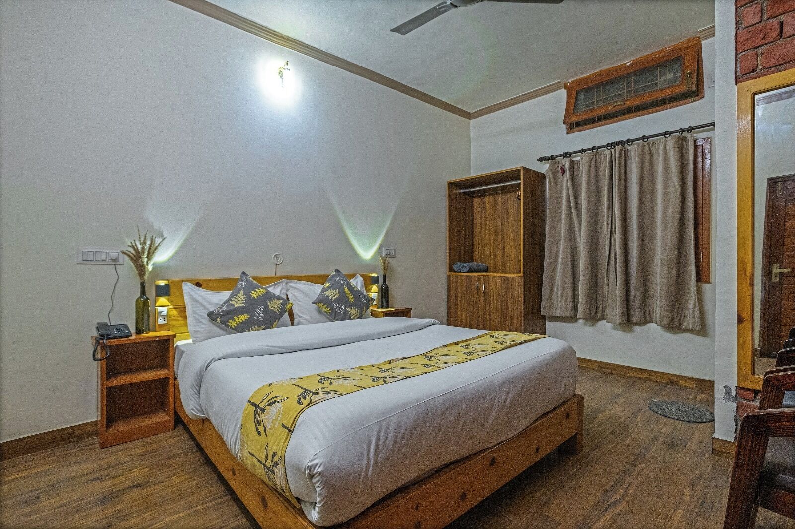 Un dormitorio con cama de madera, mesita de noche con lámpara, armario y ventana con cortinas.