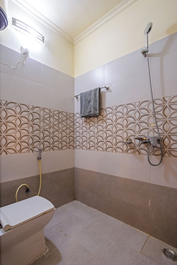 Casa de banho com sanita, chuveiro e azulejos estampados nas paredes.