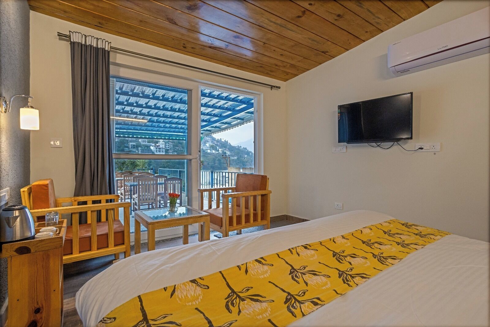 A hotel room with a bed, a TV, a balcony with a view, and a table with chairs.