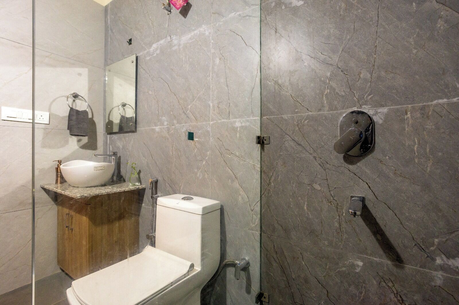 A modern bathroom with a marble wall, a white sink, a toilet, and a shower.