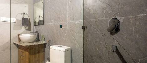 Un baño moderno con pared de mármol, un lavabo blanco, un inodoro y una ducha.
