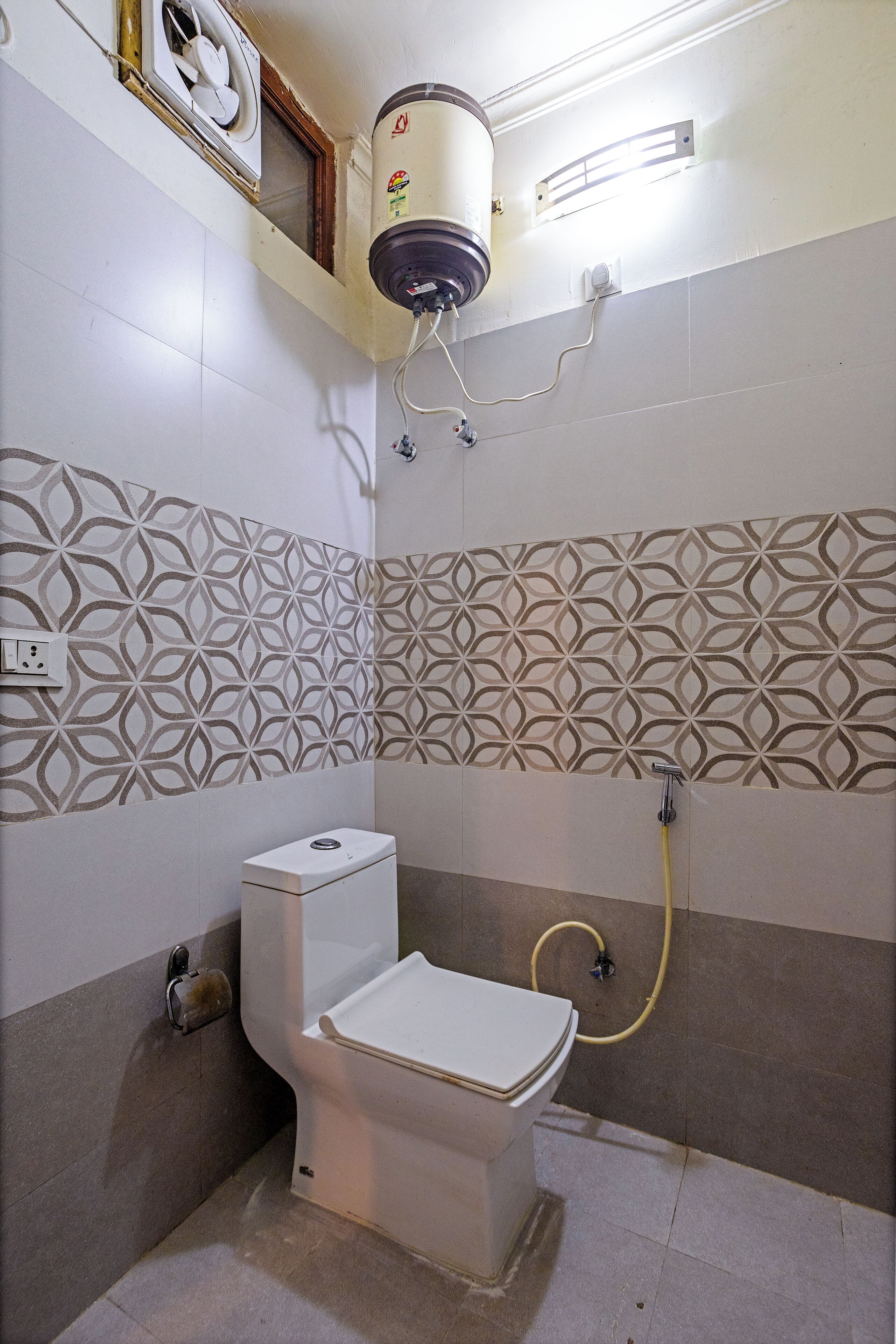 A bathroom with a toilet, a water heater, and patterned wall tiles.