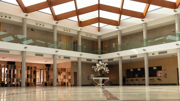 Un vaste atrium doté d’un haut plafond et d’un sol en verre, agrémenté d’un arrangement floral central et de plusieurs niveaux séparés par des rampes en verre.