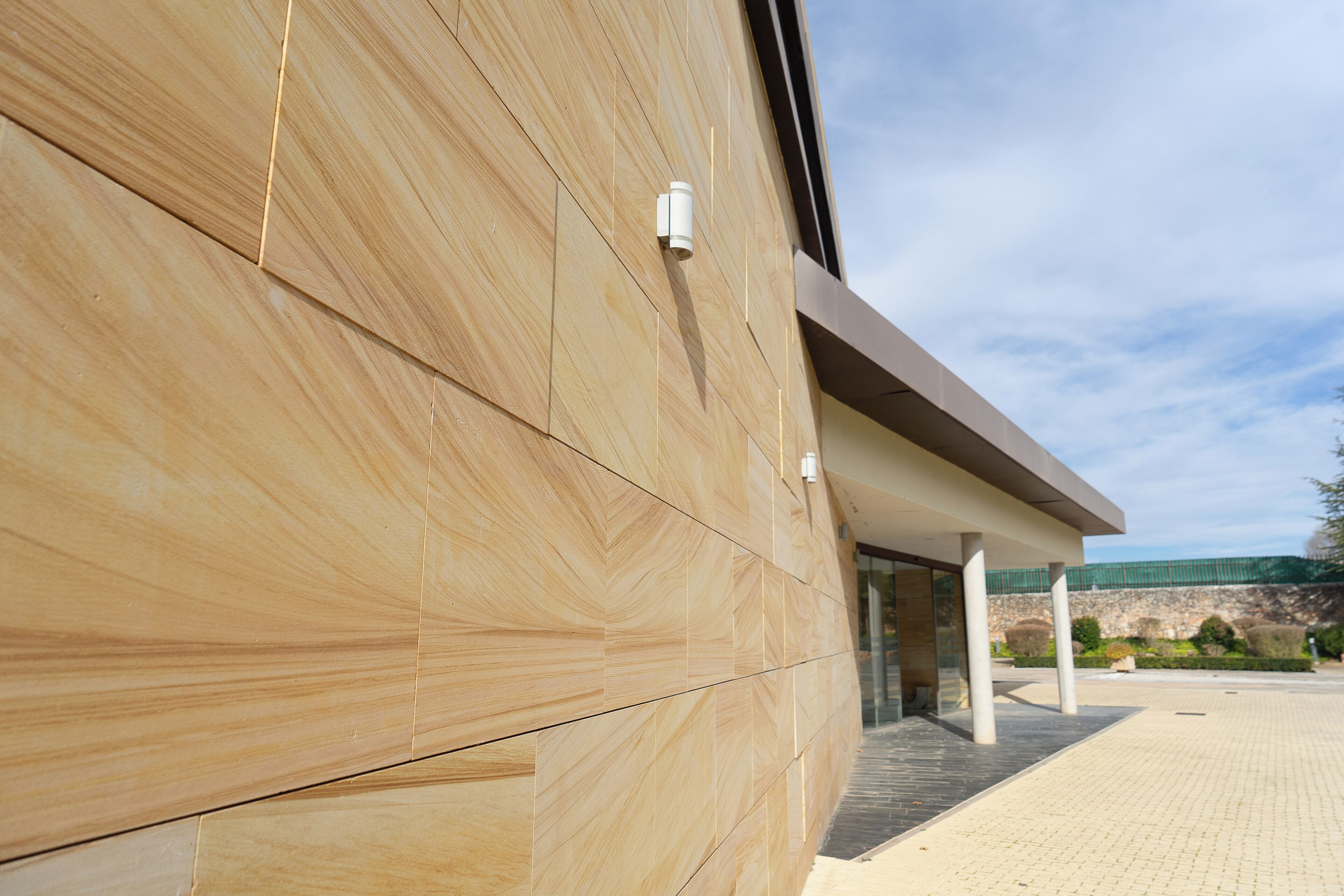A modern building facade with a curved design, large windows, and a paved entrance area.