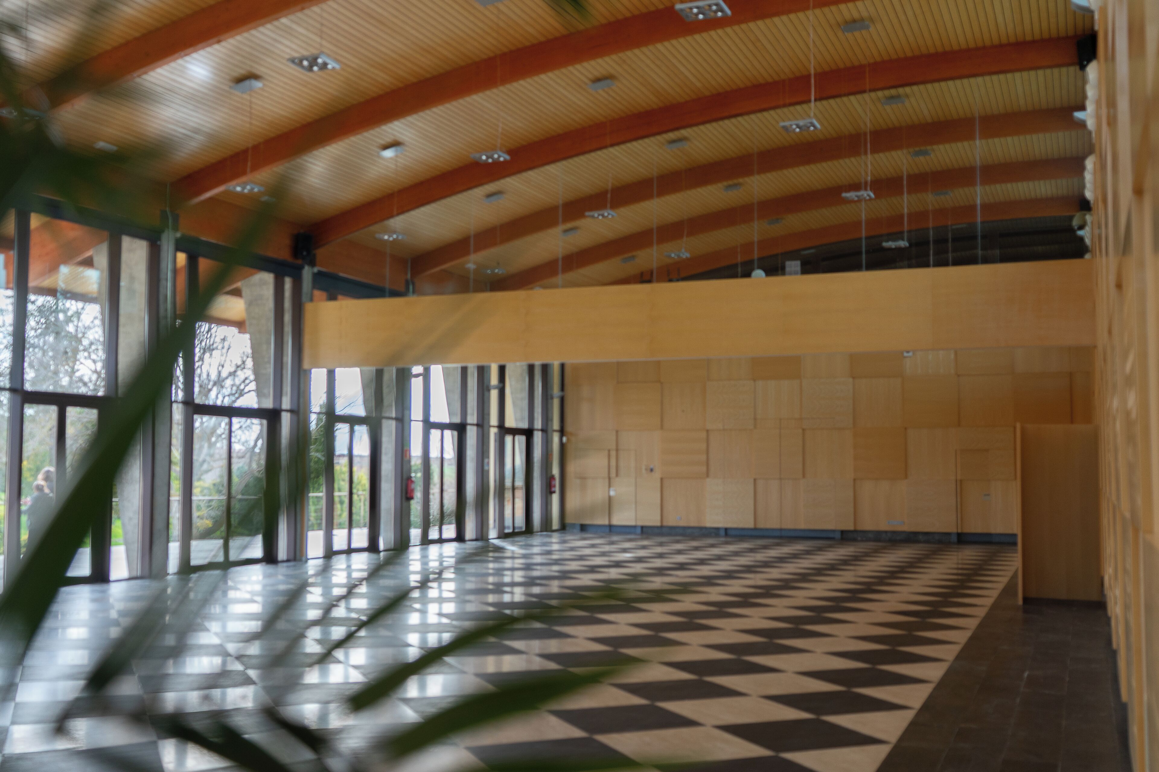 An indoor space with a checkered floor, wooden ceiling beams, and large windows.
