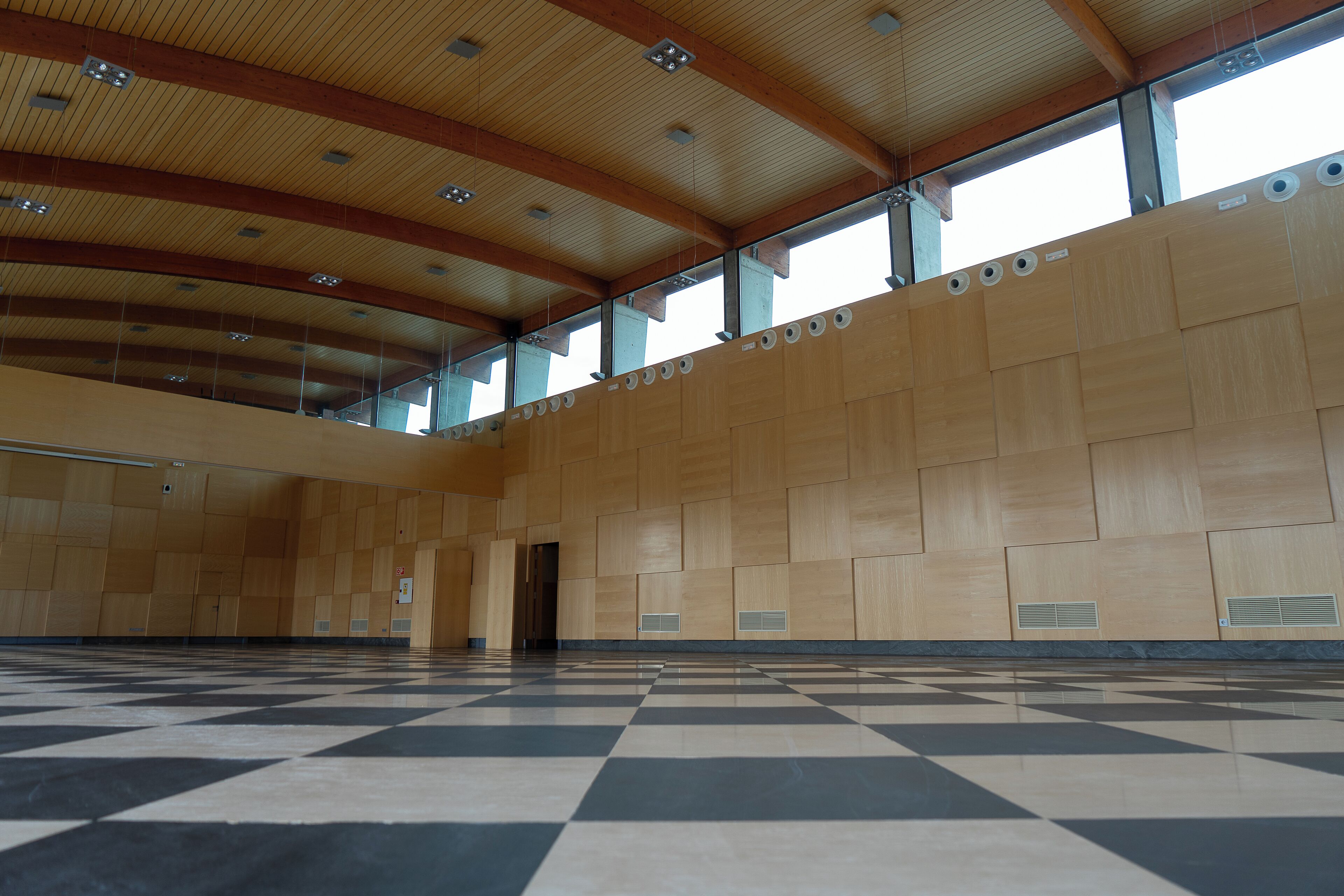 Ein geräumiger Saal mit Schachbrettmuster-Boden, Holzwandverkleidung und einer hohen Decke mit eingelassener Beleuchtung.
