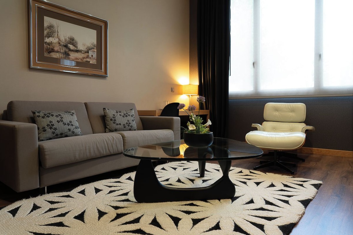 Un salon comprenant un canapé, une table basse en verre, un fauteuil, une lampe et un tableau encadré accroché au mur.