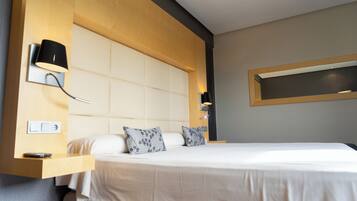 A modern hotel room with a large bed, a wooden headboard, a bedside table with a lamp, and a built-in shelf.
