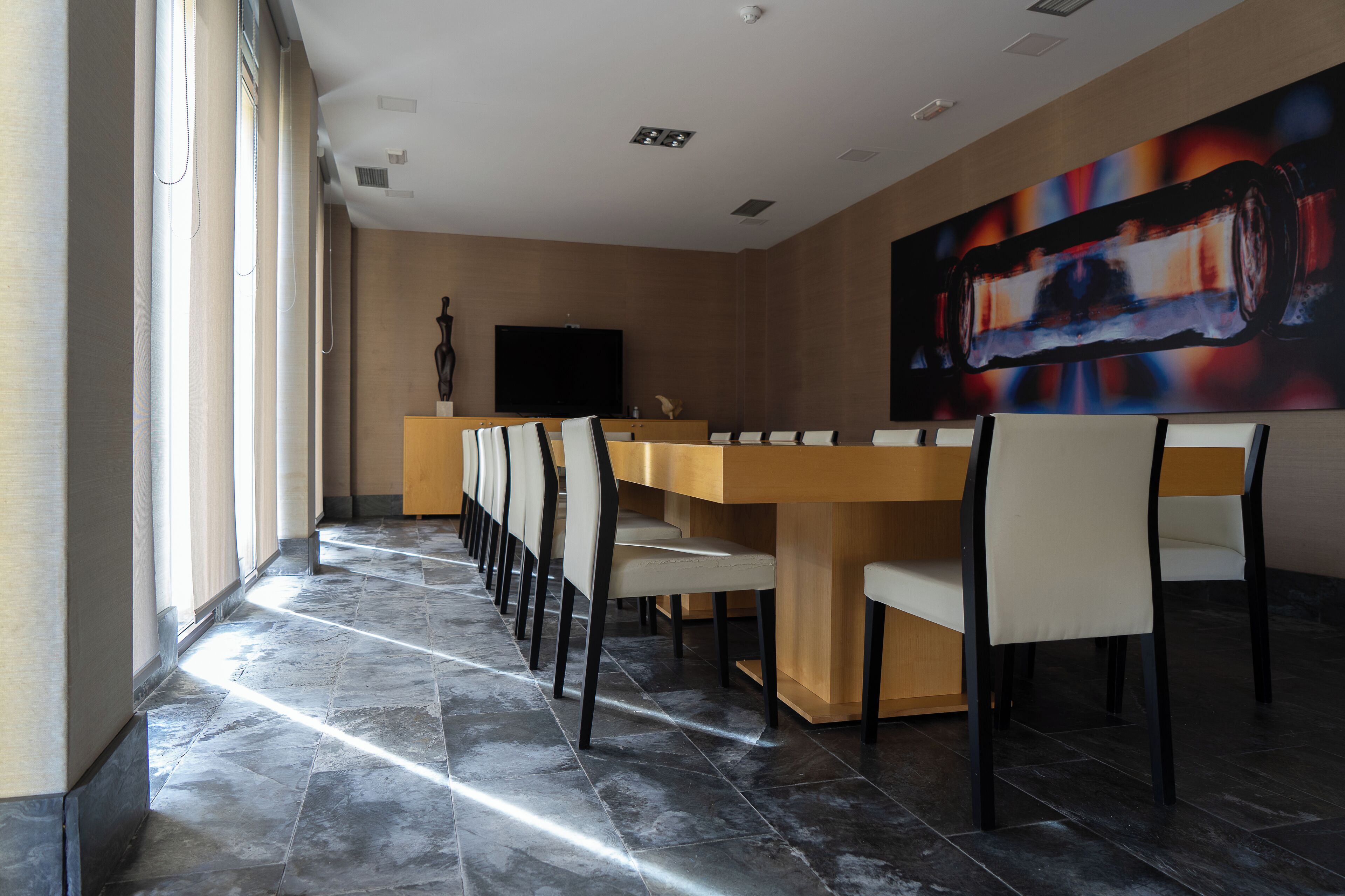 Un salón de conferencias con una larga mesa y sillas, un televisor de pantalla plana y un gran cuadro abstracto en la pared.