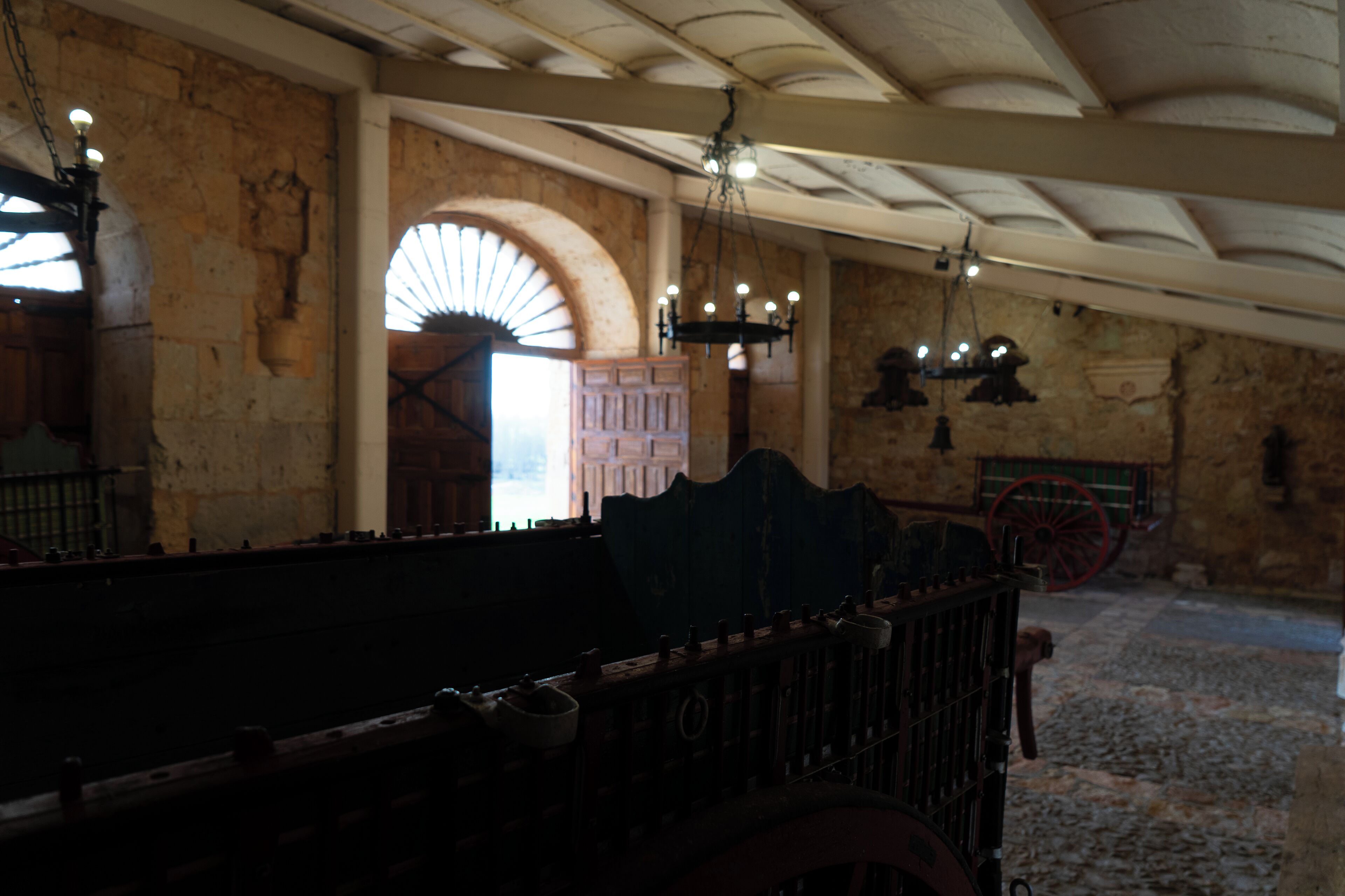 Un intérieur à la lumière tamisée, avec des murs en pierre, un banc en bois et une grande porte en arc de cercle.