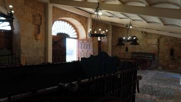 Un intérieur à la lumière tamisée, avec des murs en pierre, un banc en bois et une grande porte en arc de cercle.