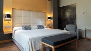 Une chambre d’hôtel moderne avec un grand lit, deux lampes de chevet, une petite table et une chaise.