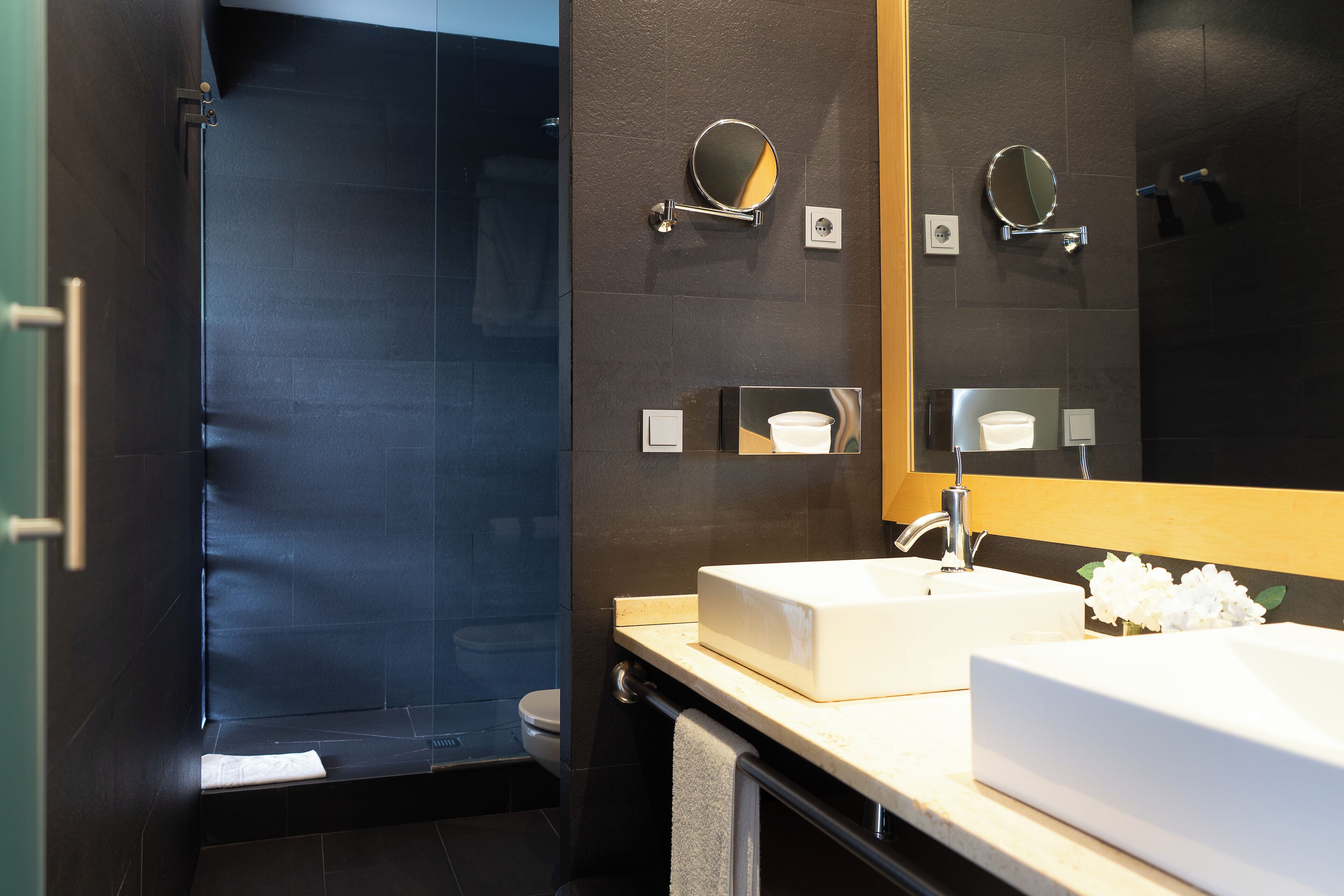 A modern bathroom with a large mirror, two sinks, and a shower area.