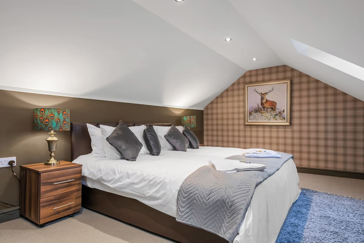 A bedroom with a large bed, a nightstand, a lamp, and a painting of a deer on the wall.