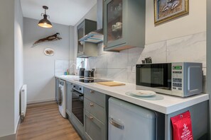 Une cuisine moderne équipée d’un four encastré, d’un micro-ondes et d’une couverture anti-feu rouge posée sur le plan de travail.