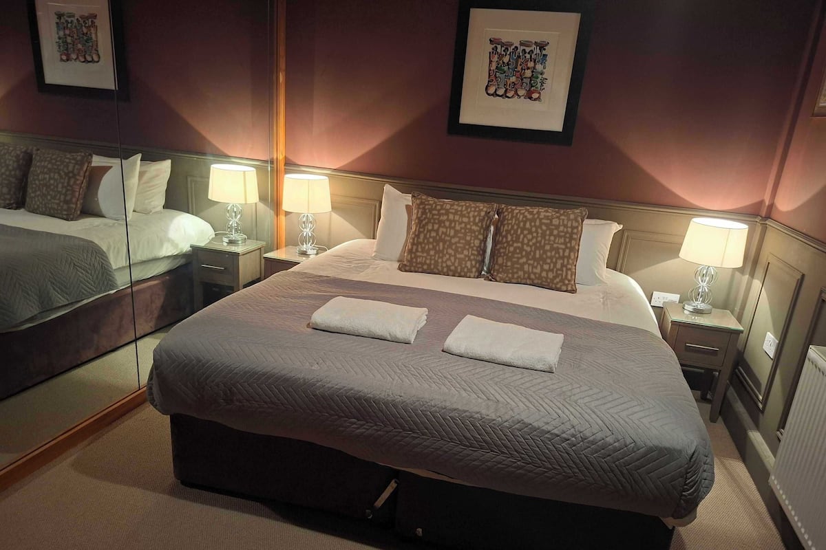 A hotel room with a large bed, two bedside tables with lamps, a mirror, and artwork on the walls.
