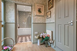 A hallway with patterned wallpaper, a checkered floor, a white radiator, and a door with a handle. -  Pools Cottages | Warwickshire Countryside Luxury (Coventry)