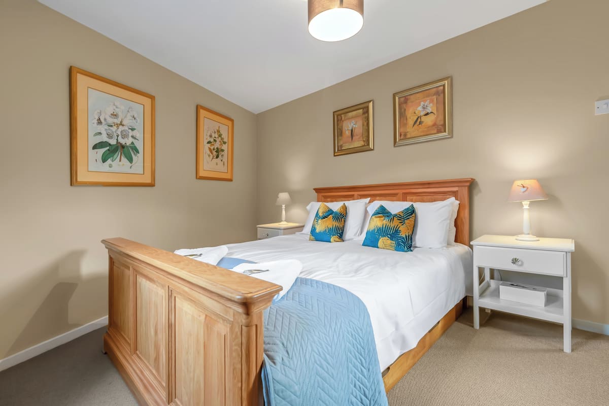 A bedroom with a wooden bed, white bedding, and three framed floral paintings on the wall.