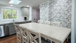 Une cuisine moderne avec un coin repas, une fenêtre donnant sur un espace verdoyant et un mur décoré d’un motif en briques.