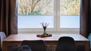 Et spiseområde med et træbord, stole, en vase med blomster og et vindue med persienner.