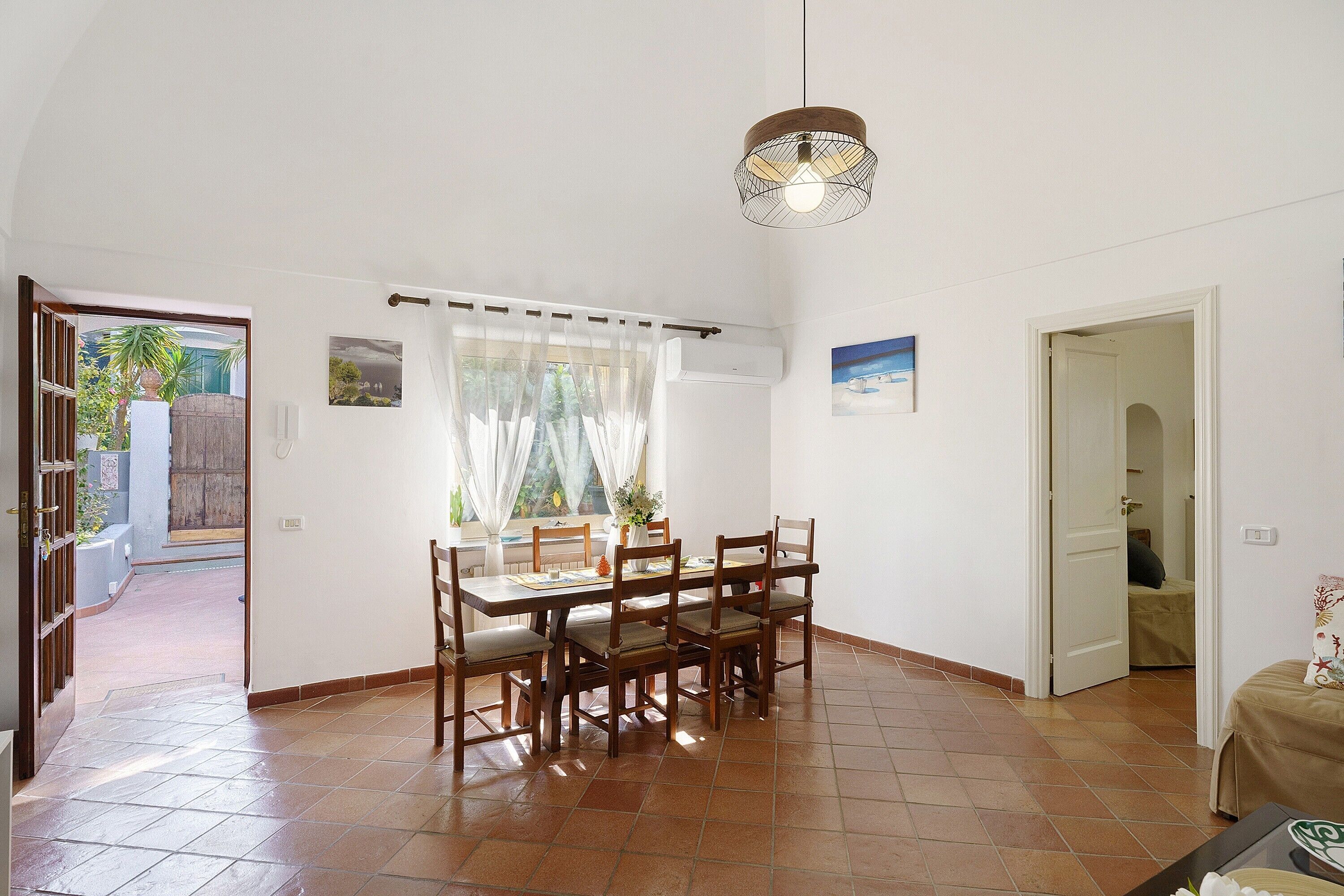 Un espace repas comprenant une table et des chaises, un luminaire suspendu et une vue par la fenêtre.