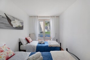 A bedroom with two beds, a view through a glass door, and a painting on the wall.