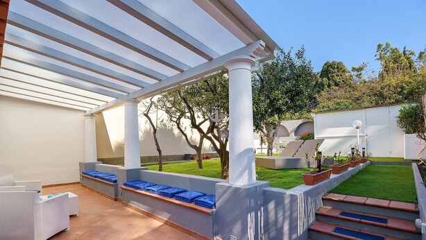 A covered patio area with a white pergola, outdoor seating, and a small garden.