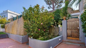 A courtyard with a wooden fence, a planter with flowers, and a building with a stone wall in the background.