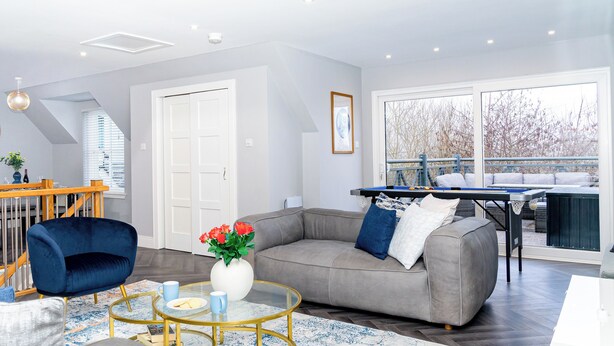 Ein modernes Wohnzimmer mit grauem Sofa, blauem Sessel, einem Glastisch und einem Essbereich mit Tisch und Stühlen.