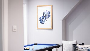 Ein Zimmer mit Billardtisch, einem gerahmten Kunstwerk mit Würfeln und einem Bett mit gemusterten Betttextilien.