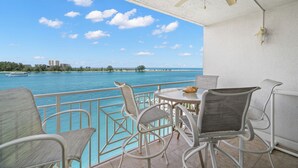 Un balcon avec vue sur la mer, des chaises blanches, une table et un ventilateur de plafond.