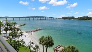 Une plage avec un pont en arrière-plan, des palmiers et une eau d’un bleu limpide.