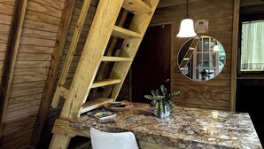 Un interior rústico de madera con techo inclinado, un espejo redondo, una mesa con una revista y una silla blanca.